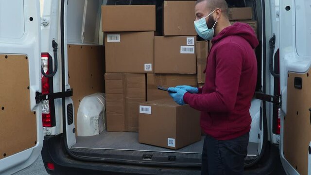 Young man courier with his van delivers a package to female recipient wearing gloves and face mask during the global pandemic from Covid-19 Coronavirus - Worker scans code with tablet