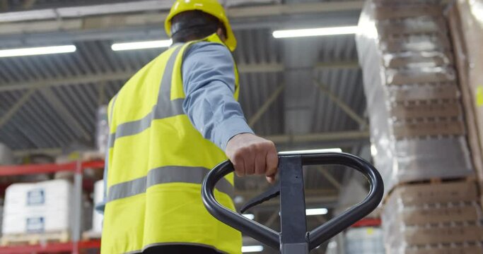 Senior worker in warehouse using hand pallet stacker to transport goods.