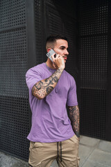 Chico joven atractivo posando con ropa de moda y usando el smartphone