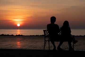 Fototapeta na wymiar silhouette couple sitting on the bench in the morning and sunrise behind them