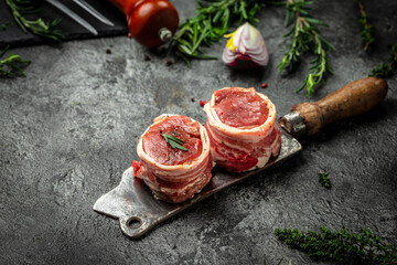 Beef tenderloin steaks wrapped in bacon erved on old meat butcher on dark concrete background. top...