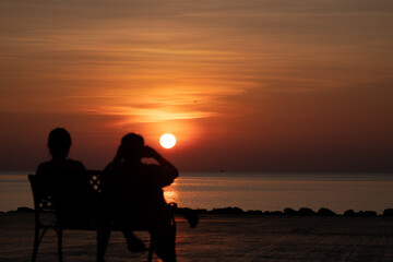 silhouette couple sitting on the bench in the morning and sunrise behind them