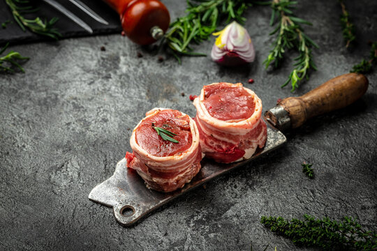 Beef tenderloin steaks wrapped in bacon erved on old meat butcher on dark concrete background. top view