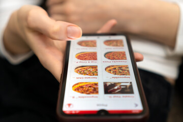 Woman holds a close-up of a mobile phone with a pizzeria website on the screen. Woman orders pizza on the phone. Food Delivery Concept