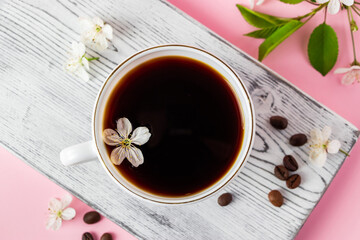 Strong espresso coffee on a white wooden tray. Spring flowers of an apple tree on a pink background. Good morning and spring time concept.