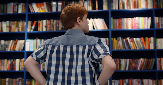 Back view of teen boy choosing book on bookshelf in library