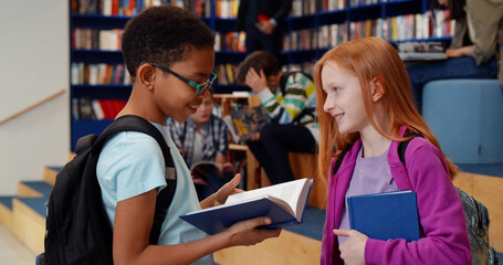 Multiethnic schoolchildren reading book and talking in library