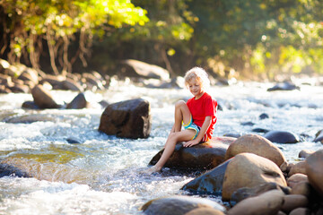 Child hiking in mountains. Kids at river shore.