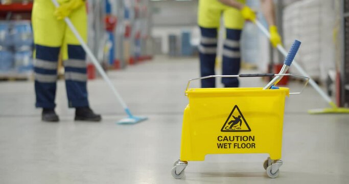Cropped shot of worker swearing safety overall holding mop cleaning floor in warehouse