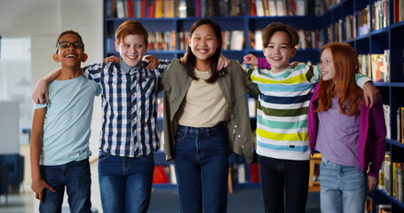 Obraz premium Portrait of multiethnic classmates hugging and smiling at camera in school library