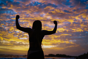 Fototapeta na wymiar Back silhouette view of satisfied fit girl celebrating sportive goals during evening time at coastline with picturesque colorful sky, carefree female athlete with casual figure feeling freedom