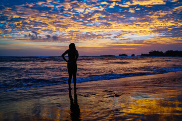 Fototapeta premium Back view of athletic trainer looking at picturesque colorful sky and seascape enjoying evening sunset at coastline, tranquil yogi in sportive wear getting energy and motivation from beautiful nature