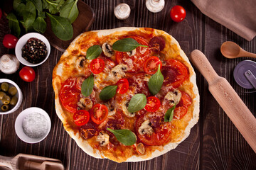 Homemade pizza with pepperoni sausage, bacon decorated spinach. Top view.