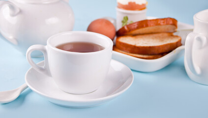 Cup of tea and boiled egg in eggcup on wooden board with crispy toast. Breakfast concept.