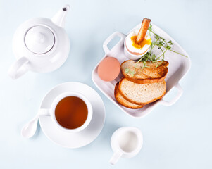 Cup of tea and boiled egg in eggcup on wooden board with crispy toast. Breakfast concept.