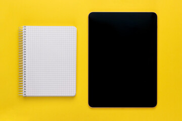 Open spiral squared notebook or notepad with blank empty white sheets and black digital tablet on bright yellow background, top view, flat lay