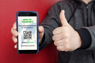 Man holds smartphone with international vaccination certificate on screen, digital vaccination passport for COVID-19, qr-code, shows thumb up. Health Passport concept, Coronavirus outbreak situation.