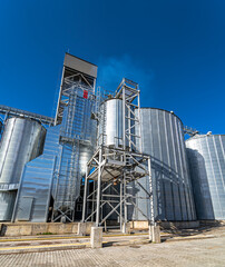 Metal grain elevator in agricultural zone. Selective focus on steel construction with blue sky above at granary. Closeup.