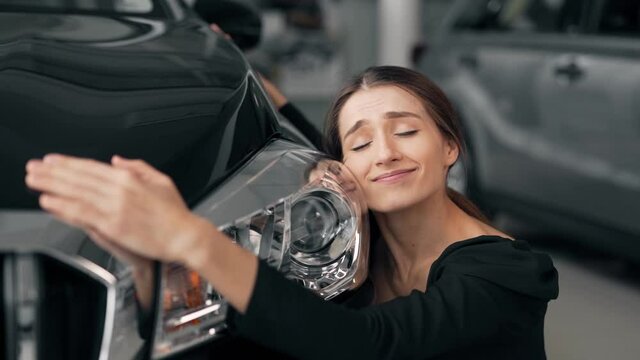 Close-up of a beautiful happy girl who hugs a new car and kisses