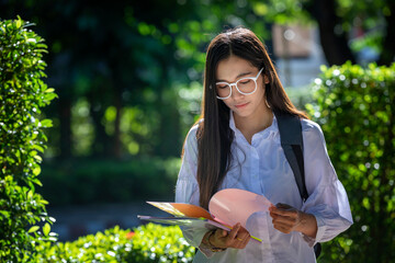 Beautiful female Asian students in trendy clothes chatting on their smartphones to plan their leisure travel. In your mobile phone, documents and notebooks, get ready to record events.