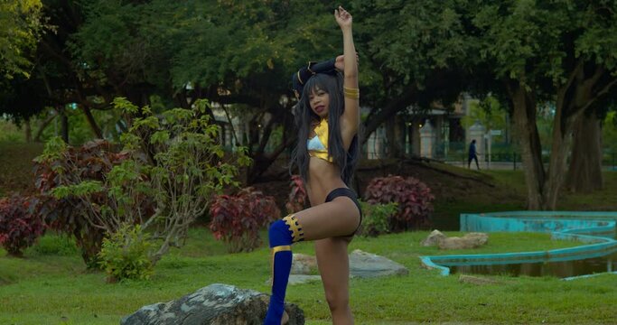 Sexy Ishtar Goddes cosplay costume girl standing in a garden with a manmade pool in the background