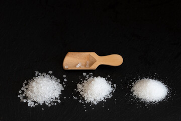 gross and fine white sea salt and a wooden scoop black background