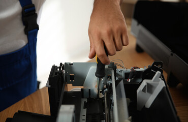 Repairman with screwdriver fixing modern printer indoors, closeup