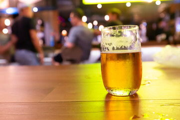 Beer in the short glass on the table at night bar with background people meeting in the club. Hang out concept.