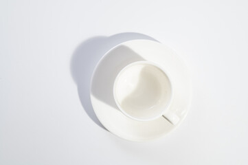empty white cup and saucer on white background, hard light, shadow, top view