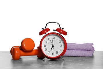 Alarm clock, towels and dumbbells on marble table against grey background. Morning exercise
