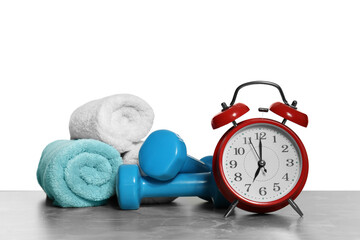 Alarm clock, towels and dumbbells on marble table against grey background. Morning exercise