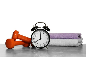 Alarm clock, towels and dumbbells on marble table against grey background. Morning exercise