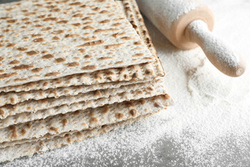 Stack of traditional matzos, rolling pin and flour on table, closeup