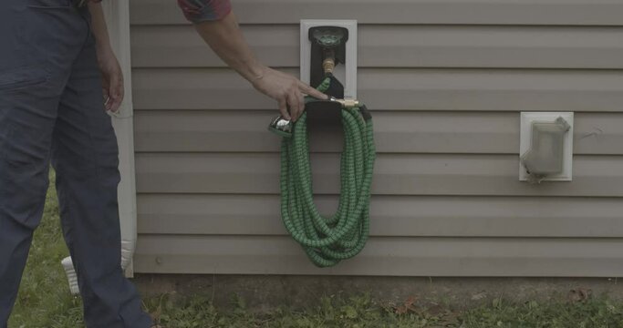 Male neatly storing a garden hose on an outdoor faucet.