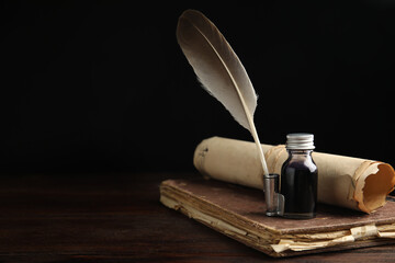Feather pen, bottle of ink, old book and parchment scroll on wooden table. Space for text