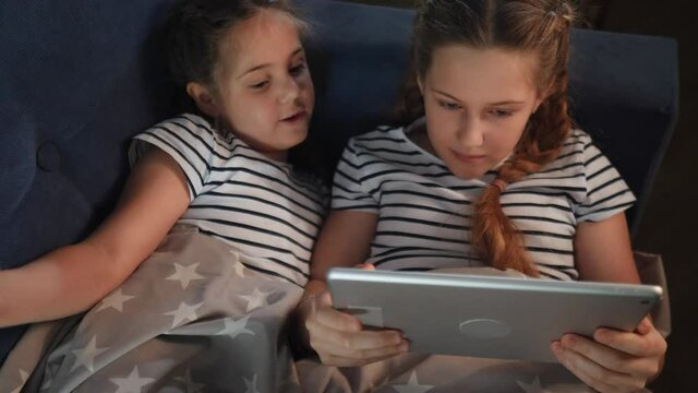two kids girls on the couch at night with a digital tablet network. kid dream online video games at concept. daughters kids watching online video on the couch at night with digital tablet