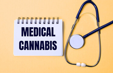 On a beige background, a stethoscope and a white notepad with the inscription MEDICAL CANNABIS. Medical concept