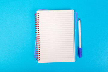 stack of school exercise books on blue background, spiral notepad with blank page and pen on table...