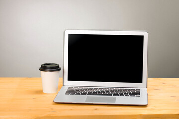 Fototapeta premium Mockup blank laptop screen with coffee on wooden table in coworking space.