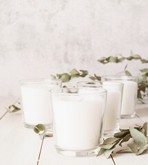 Fototapeta na wymiar Beautiful white burning candles with eucalyptus leaves on white wooden background