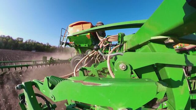 Close up of tractor with harrow system plowing ground on cultivated farm field, pillar of dust trails behind, preparing soil for planting new crop
