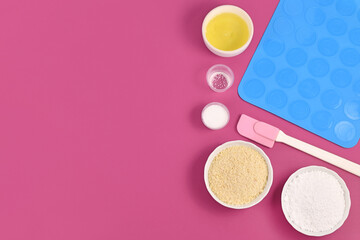 Ingredients for making homemade French Macaron sweets including powdered sugar, ground almonds, egg white, salt and baking tools like mold mat and icing pipe on pink background