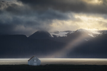 Fototapeta na wymiar House on the coast in Northeast Iceland. Sun ray through the clouds from the sky. Mountains nature landscape at sunset
