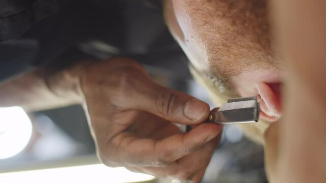 Close up vertical shot of hand of black barber using straight edge razor while shaving beard of male client in barbershop