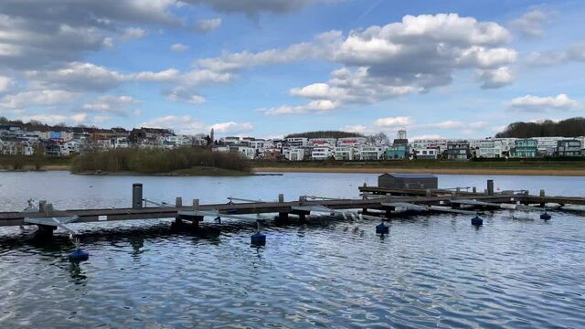 Pan shot of wooden dock of Phoenix Lake in Dortmund with luxury villas on shore in background. Dortmund City,Germany.