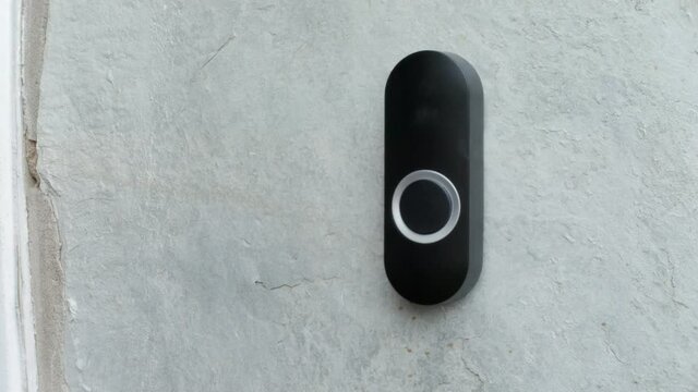 House door bell being pressed. A woman presses a black doorbell with her finger on a stone wall.