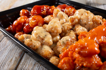 A closeup view of a to-go container of assorted flavors of boneless chicken wings.
