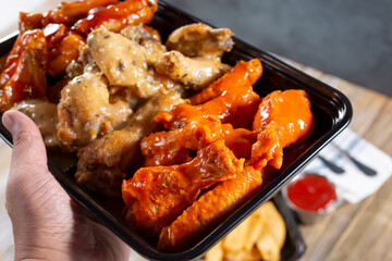 A view of a hand holding a to-go container of assorted chicken wings.