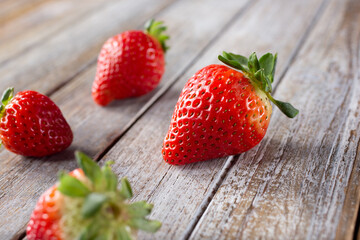 A view of several strawberries scattered around a wood table surface.