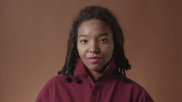 Lockdown of young African-American woman with problem skin and stylish dreads on her head wearing shirt fixing its collar while looking at camera and smiling